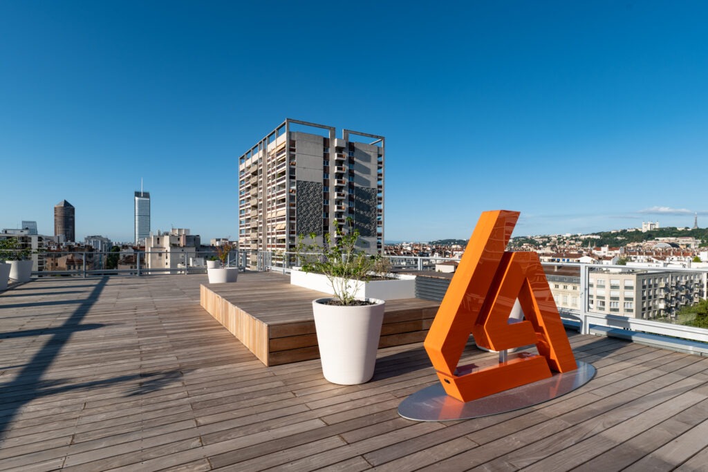 Auxiliaire BTP rooftop avec ciel bleu et logo Auxiliaire BTP orange et terrasse en bois